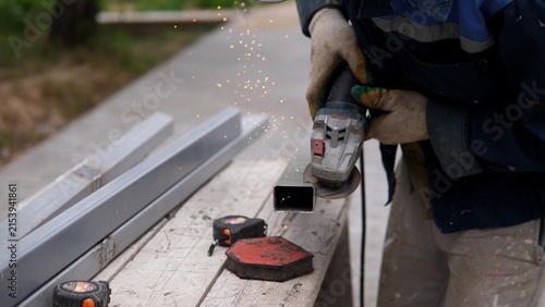 Foto Industrial worker grinding metal square tubing with handheld power tool, sending