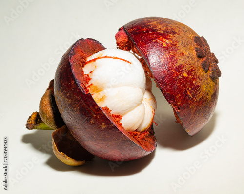 Cut mangosteen (Garcinia mangostana) fruit opened in half showing rich purple rind and juicy white internal segments on a light background