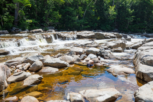 Swift River cascading over a rocky ledge into clear wading pools at the Lower Falls Scenic Area in White Mountain National Forest, New Hampshire.