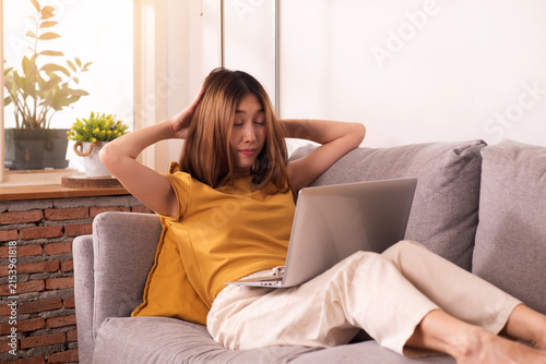 Tired woman working from home on laptop, experiencing work fatigue from prolonged screen time and sedentary work on a sofa.