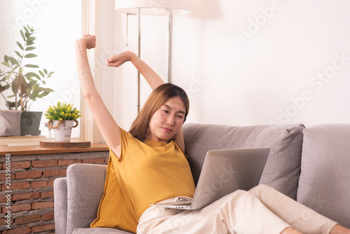 Tired woman working from home on laptop, experiencing work fatigue from prolonged screen time and sedentary work on a sofa.