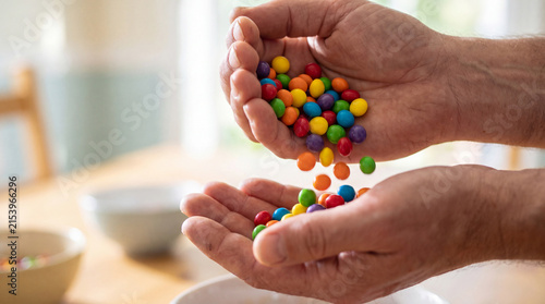 Fotografía Two adult hands cupping a generous handful of brightly colored, sugar-coated candies, with a few falling down