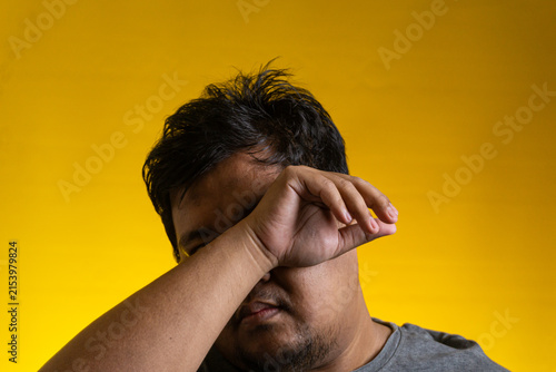 Fotografie A raw and expressive portrait of a young Asian male pressing his forearm against his eyes to hide his face