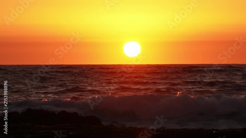 Slow motion of an ocean wave crashing against rocks and kelp during a golden sunset, backlit silhouette with copy space.