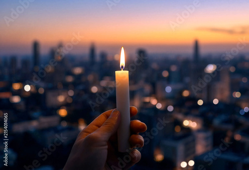 Hand holding a lit candle against a stunning cityscape skyline during twilight or sunset hour