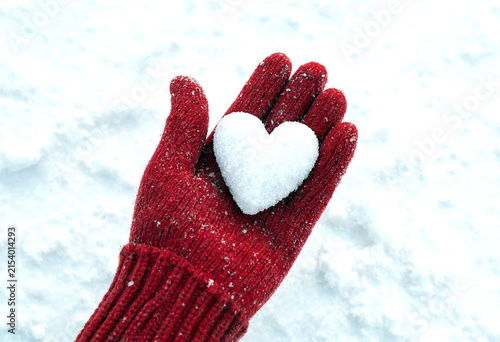 Heartshaped snowball carefully held in a red woolen mitten on snowy ground