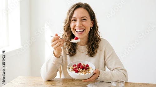 Happy young woman eating a healthy bowl of granola with fresh red berries for breakfast
