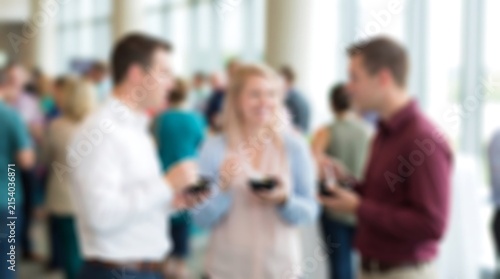 Group of business professionals standing in office corridor during networking event having snacks and drinks with soft sunlight streaming through floor to ceiling windows nearby