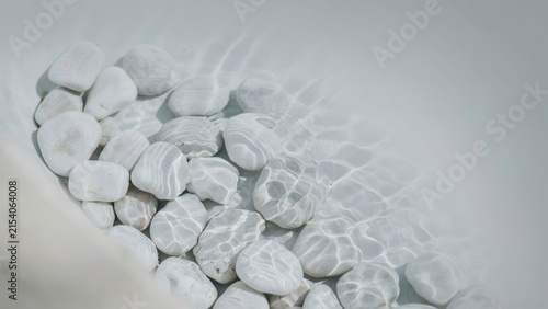 Smooth white river stones resting underwater in a clear basin with rippling light patterns dancing across the surface of the submerged rocks