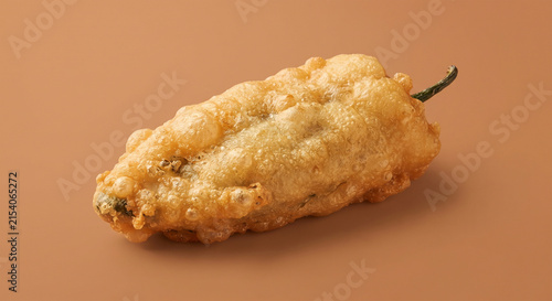  A clean, studio-lit commercial photograph of a single classic chile relleno isolated against a solid warm-earth background, emphasizing its puffy, golden-brown fried exterior and rich texture.