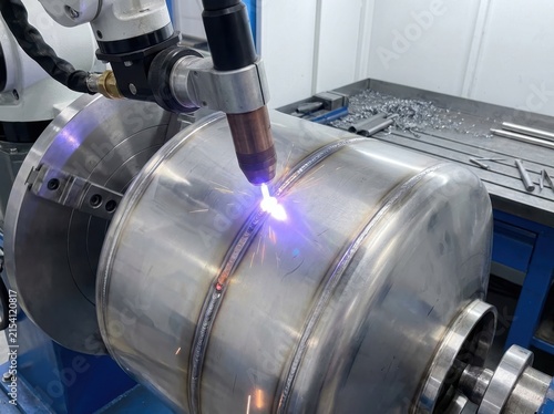 Close up of precision welding on stainless steel cylinder with sparks and flame in industrial workshop setting