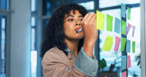 Sticky notes, glass wall and businesswoman in office with planning for creative project ideas. Board, writing and magazine editor brainstorming with research for article at startup workplace.