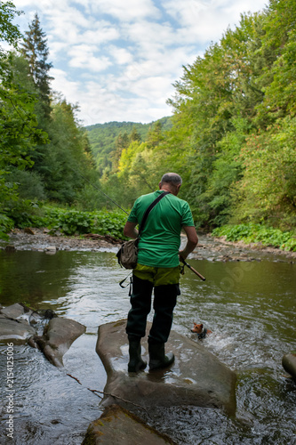 A man fishes with his dog on a scenic forest river in a pristine environment.