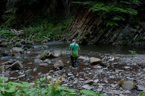 A man fishes with his dog on a scenic forest river in a pristine environment.