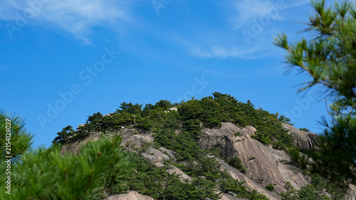 Rocky mountain peak with green pine trees under a clear blue sky framed by pine branches, South Korea