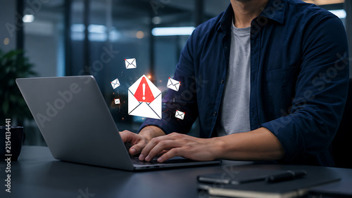 Cybersecurity alert concept featuring a male professional typing on a laptop computer with warning envelope icons floating nearby in an office setting