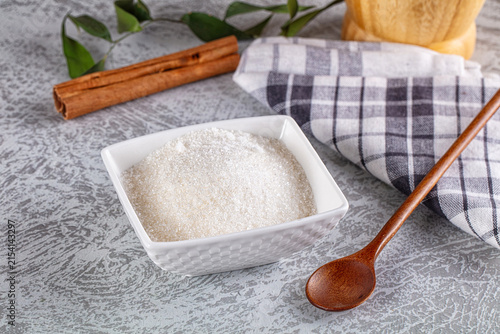 Obraz na płótnie White sugar in ceramic bowl with cinnamon sticks and wooden spoon on textured su