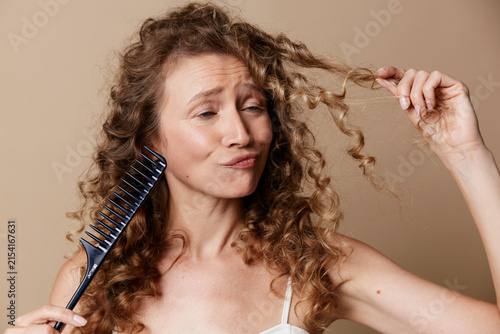 Fotografie Natural middle aged woman with curly hair, unretouched skin, holding a comb, candid beauty, selfcare moment, routine grooming, warm studio light