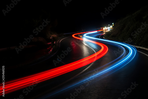 Long exposure photograph captures winding road with vibrant red and blue light trails at night automotive transportation nighttime roadway highway curve light painting streak motion blur