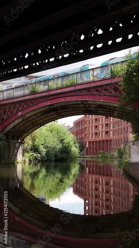Red bridge and apartment buildings reflecting in the canal in Manchester at midday