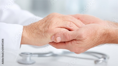 doctors hands in white sleeves holding the hand of a senior patient during a medical consultation. Focus on the connection between the hands with a blurred stethoscope in the background. High 
