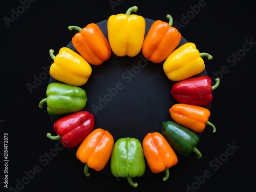 Colorful red, yellow, orange, and green bell peppers arranged in a ring on a dark slate background.