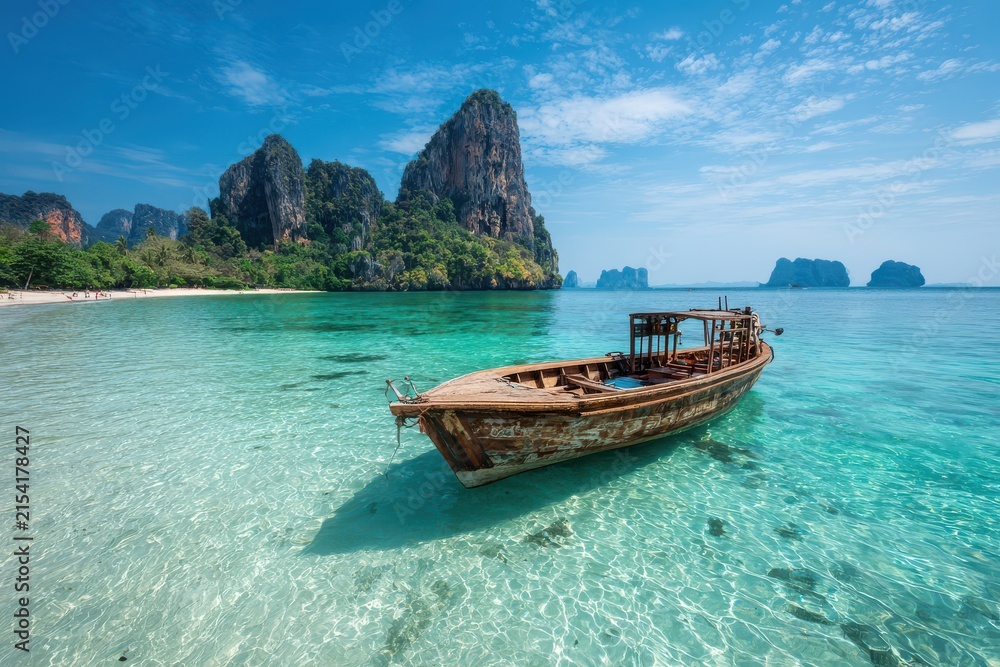 Obraz premium Wooden boat floating in clear turquoise water with limestone karsts and tropical beach background