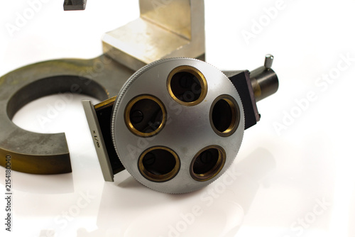 Close-up of a vintage microscope objective turret with multiple lens positions and mechanical adjustment components, photographed against a white background.
