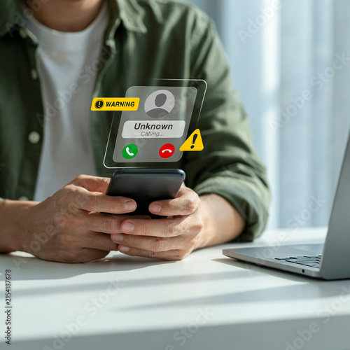 Man holding a smartphone receives a suspicious spam call warning from an unknown caller while at his desk.
