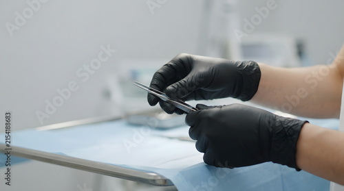 Surgeon hands in black nitrile gloves holding a metal surgical tool over a sterile tray in a clinic