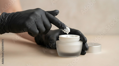 Close-up of a gloved hand dipping a finger into a jar of white cream, suggesting skincare or cosmetic application