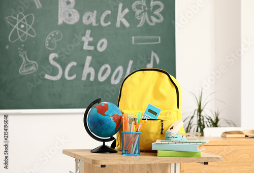 Yellow backpack with school supplies, globe, and books on a desk in front of ...