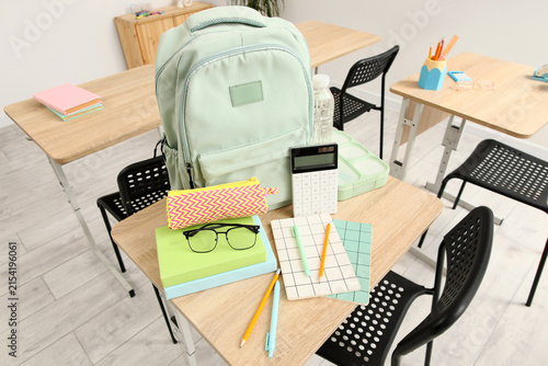Mint green backpack and school supplies on a wooden desk in an empty classroo...