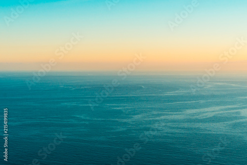 Quadro su tela Aerial view of calm blue ocean water surface during sunset horizon