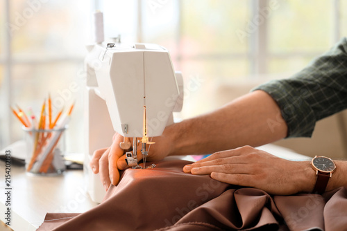 Konstfotografi Young male tailor using sewing machine in atelier, closeup