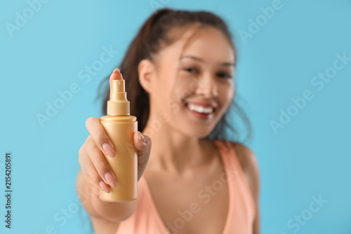 Young Asian woman with sunscreen cream on blue background, closeup