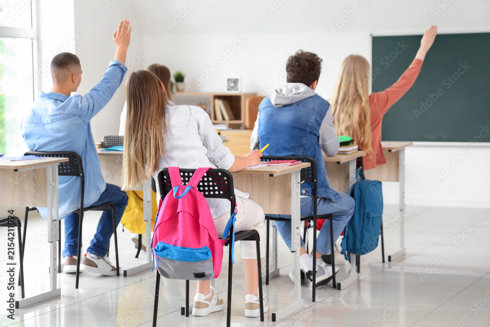 Fototapeta premium Classmates raising hands to answer in classroom