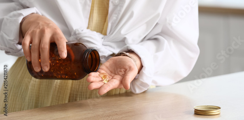 Person pouring omega-3 fish oil capsules from a brown bottle into their hand for daily health supplements