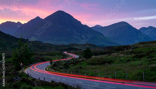 Red taillight trails on a curved road in Glencoe at dusk, quiet valley, dramatic mountain silhouettes, long exposure photography