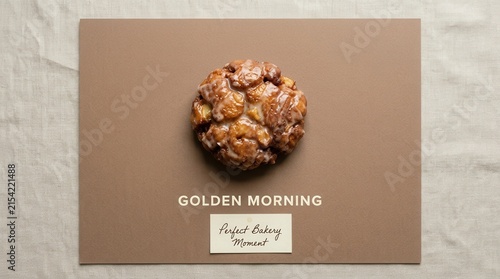 Fresh glazed apple fritter pastry rests on a brown minimalist card with golden morning text and a bakery label on a linen fabric background, perfect for breakfast themes and food marketing designs