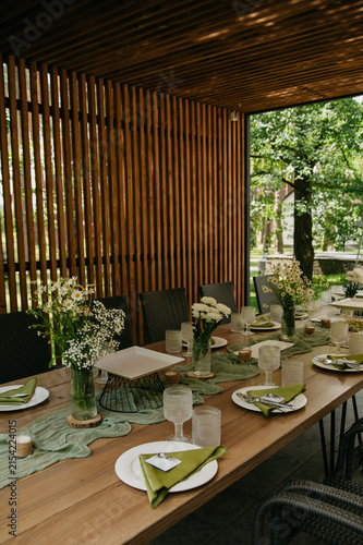 Interior of a banquet hall in the form of a gazebo in an open space with dishes, food, drinks and flowers in vases and a green tablecloth on the table for a wedding or anniversary celebration