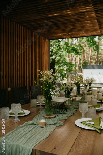 Interior of a banquet hall made of wood in the form of a gazebo in an open space with tables with dishes, food, drinks and flowers in vases for a wedding or anniversary celebration