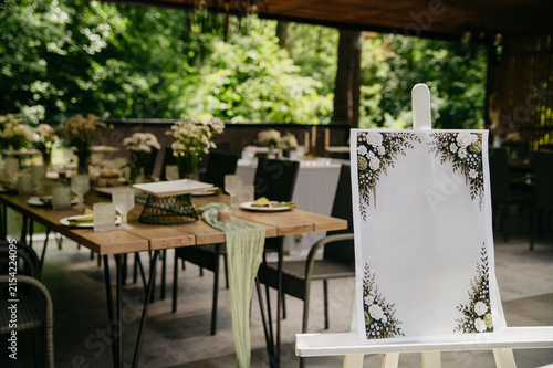 The interior of a banquet hall made of wood in the form of a gazebo in an open space with tables set with dishes, food and drinks for a wedding or anniversary celebration, with seating for guests 