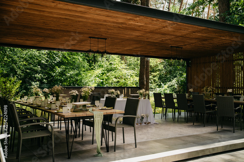 Interior of a banquet hall made of wood in an open space with tables set with dishes, food and drinks for a wedding or anniversary celebration