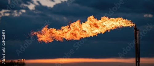 Bright orange flames erupt from an industrial pipe against a dramatic twilight sky