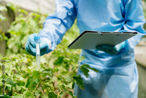 Scientist in protective gear recording crop health data on a clipboard in an outdoor agricultural r