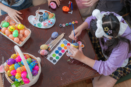 Принти на полотні At a wooden coffee table strewn with brushes, paints and eggs, a modern multicultural family of a mother and three excited young daughters adding colored dots to a hand-painted Easter egg