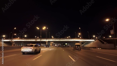 Night urban freeway beneath illuminated interchange with cars and freight truck