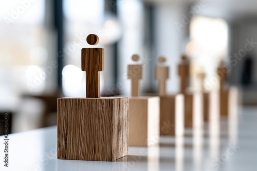 Wooden human figures arranged on blocks symbolizing leadership and hierarchy with focus on the foremost figure in a professional setting