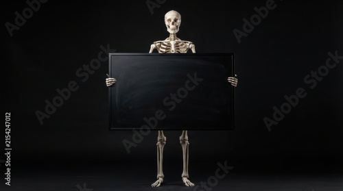 Skeleton holding blank black sign on dark background setup